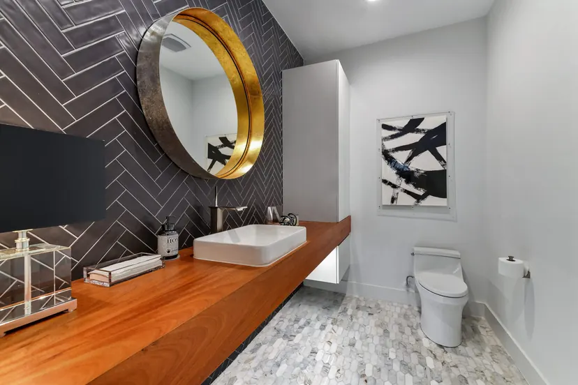 Grapevine bathroom remodel idea: floating wood vanity, round brass mirror and a charcoal herringbone wall