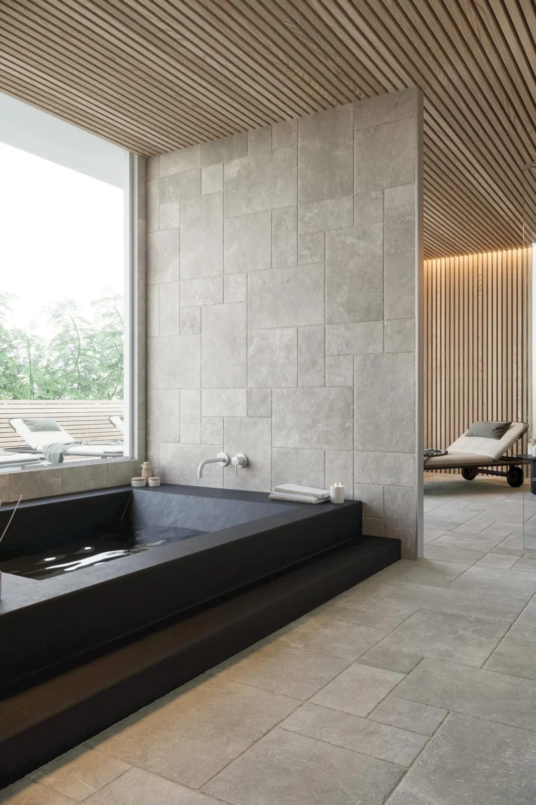 Black stone soaking tub set into a gray stone wall under a wood slat ceiling, by Nomi