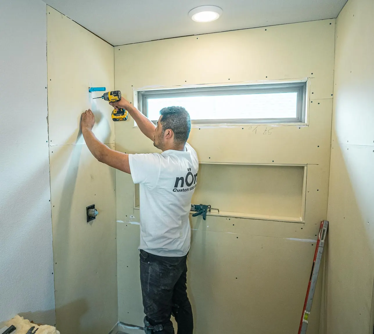 Nomi crew member fastening board to a shower wall around a window and a long niche, before waterproofing