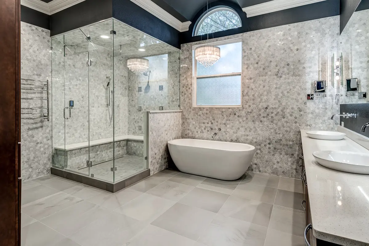 Steam shower by Nomi with a frameless glass enclosure and bench, next to a freestanding tub and marble mosaic walls